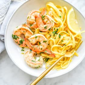a shallow white bowl filled with gluten free noodles and shrimp scampi