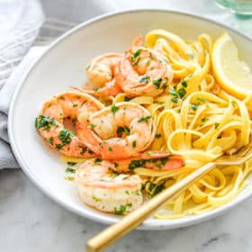 a shallow white bowl filled with gluten free noodles and shrimp scampi