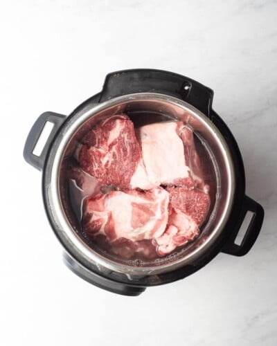 an instant pot of water and chunks of raw pork shoulder in it