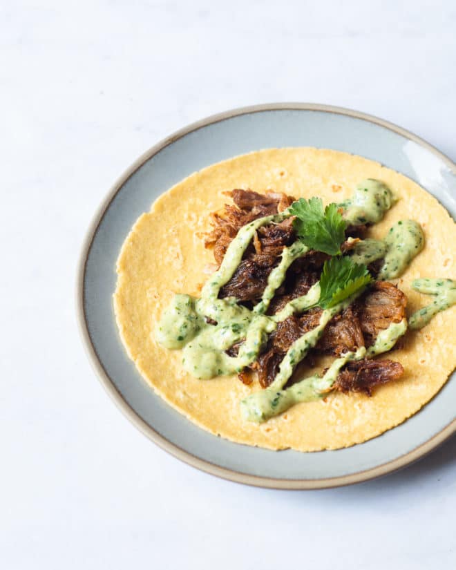a single carnitas taco topped with creamy avocado verde sauce and cilantro sitting open on a small blue plate