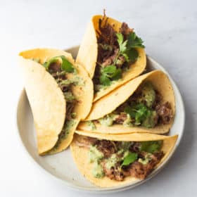 a plate of 4 carnitas tacos topped with creamy avocado verde sauce and cilantro