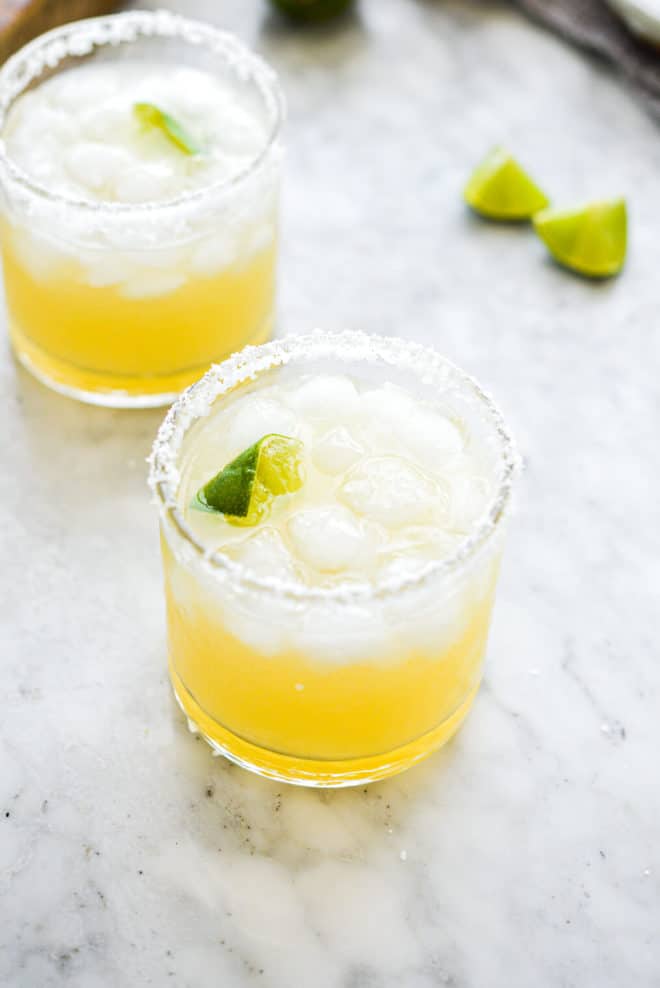 two salt rimmed glasses filled with margarita in front of sliced limes