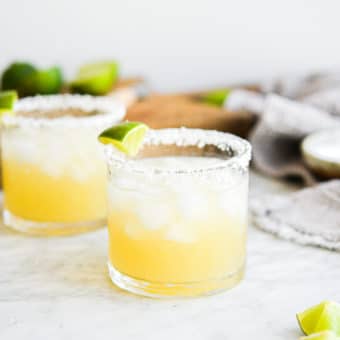 two salt rimmed glasses filled with margarita in front of sliced limes