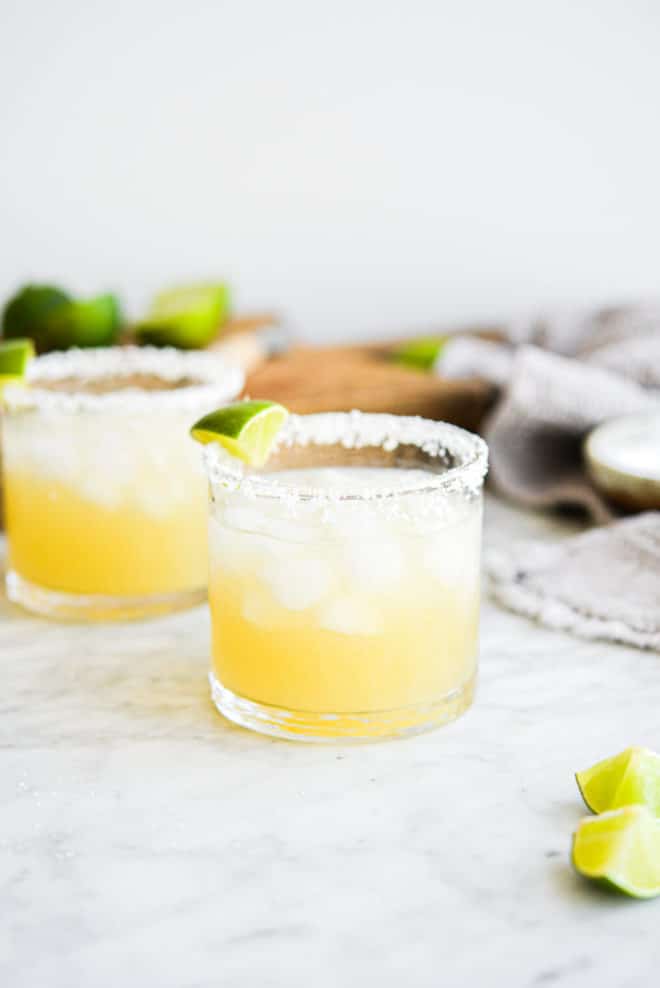 two salt rimmed glasses filled with margarita in front of sliced limes