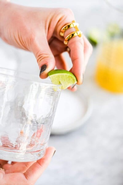 a woman squeezing lime juice around the rim of a margarita glass before salting it