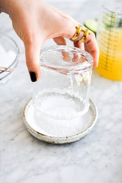 a woman's hand salting the rim of a margarita glass