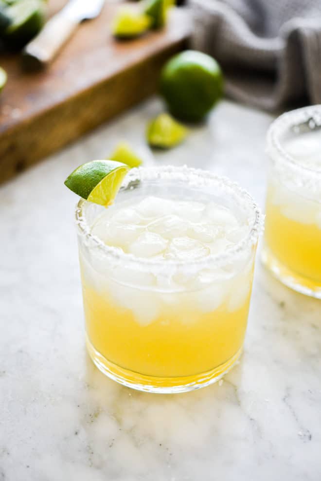 two salt rimmed glasses filled with margarita in front of sliced limes