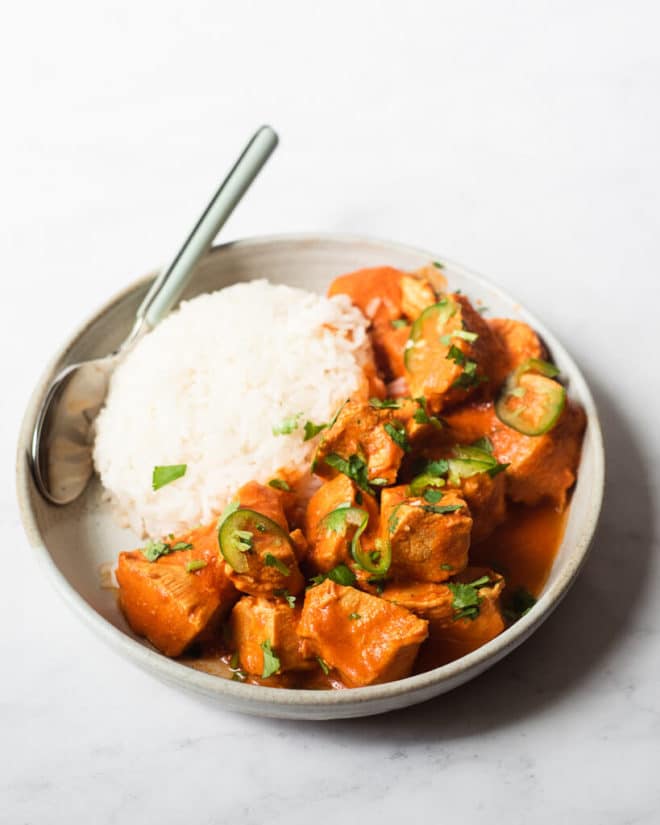 a plate of tikka masala and a bed of rice with a spoon resting on the plate