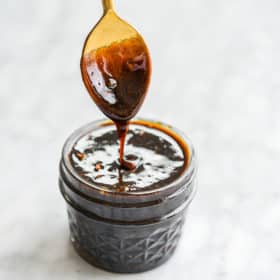 a jar of gluten free teriyaki sauce with a person holding a spoon smothered in teriyaki sauce