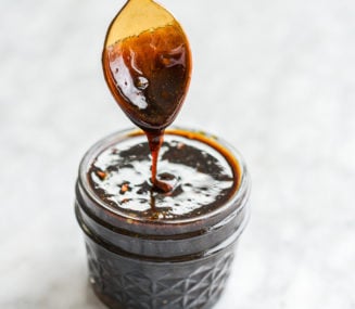 a jar of gluten free teriyaki sauce with a person holding a spoon smothered in teriyaki sauce