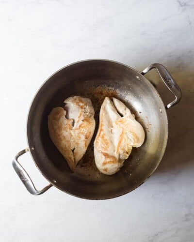 a large pot with two browned chicken breasts in it