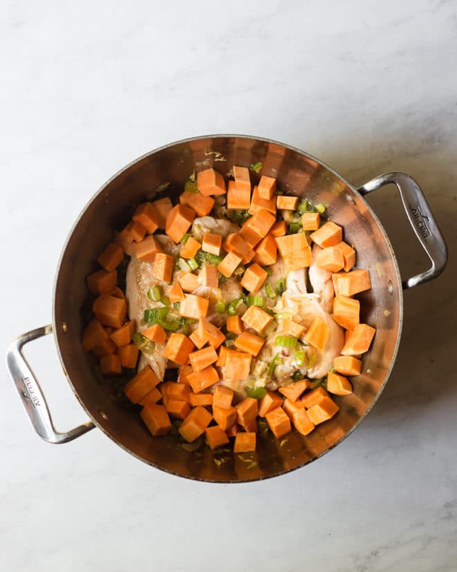 a large stainless steel pot with chicken, cubed sweet potatoes, and celery in it