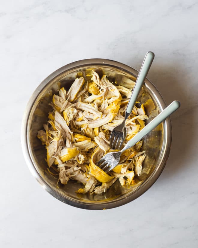 a bowl of shredded chicken slightly yellow from turmeric and two forks sticking out of the bowl