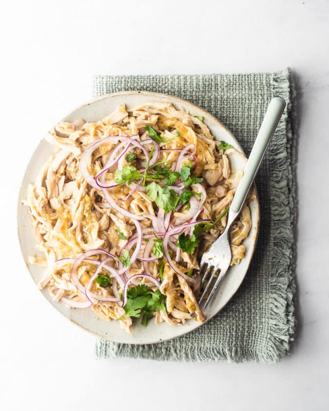 a plate of shredded salsa chicken garnished with cilantro and purple onion sitting on a green kitchen towel