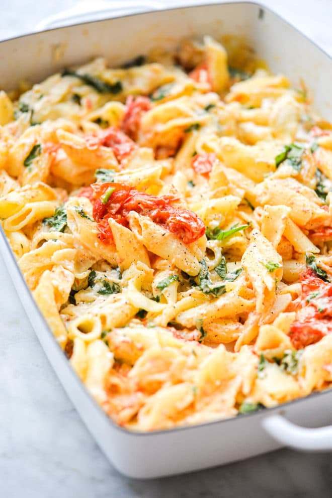 a white baking dish of baked feta pasta sitting on a marble surface