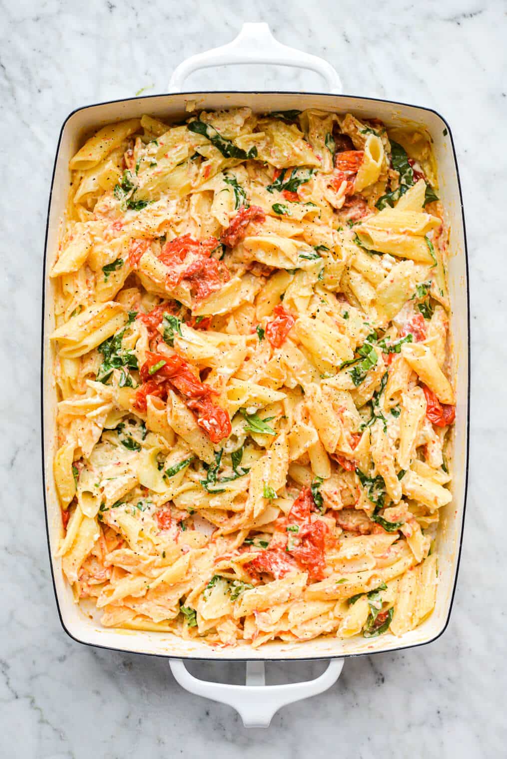 a white baking dish of baked feta pasta sitting on a marble surface