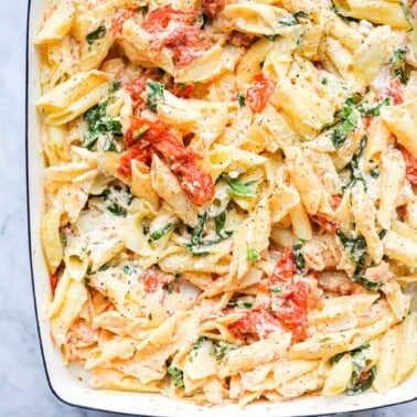 a white baking dish of baked feta pasta sitting on a marble surface