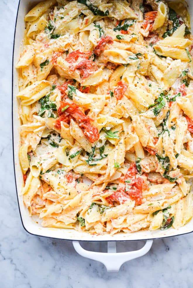 a white baking dish of baked feta pasta sitting on a marble surface