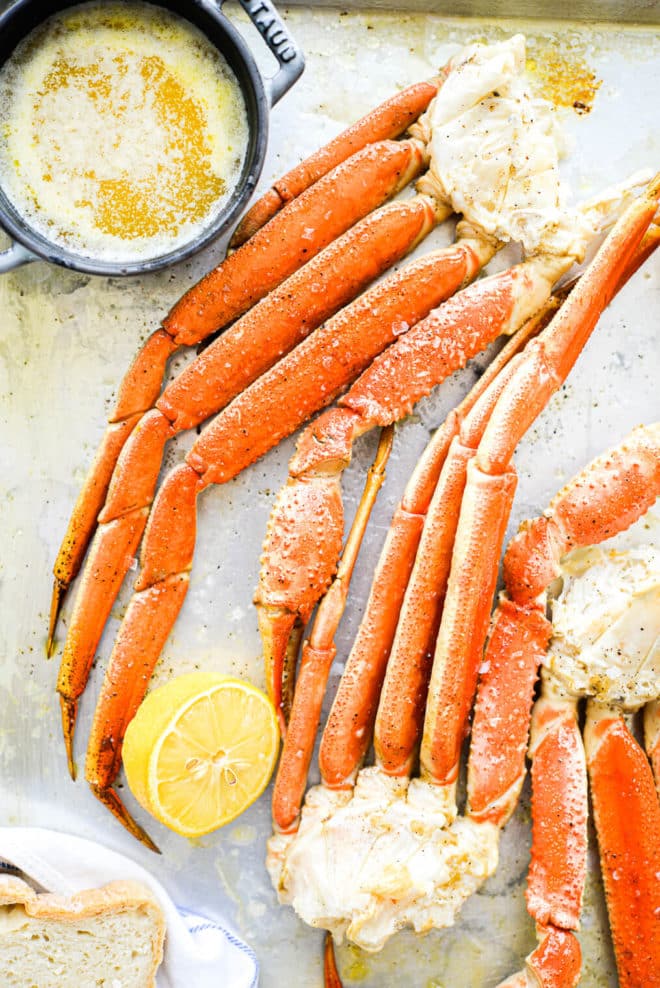 a crab bake sheet pan with halved lemons, crab legs, and butter on it