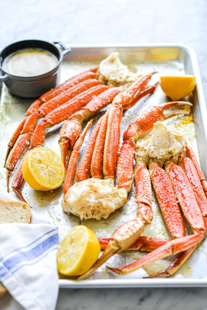 a crab bake sheet pan with halved lemons, crab legs, and butter on it
