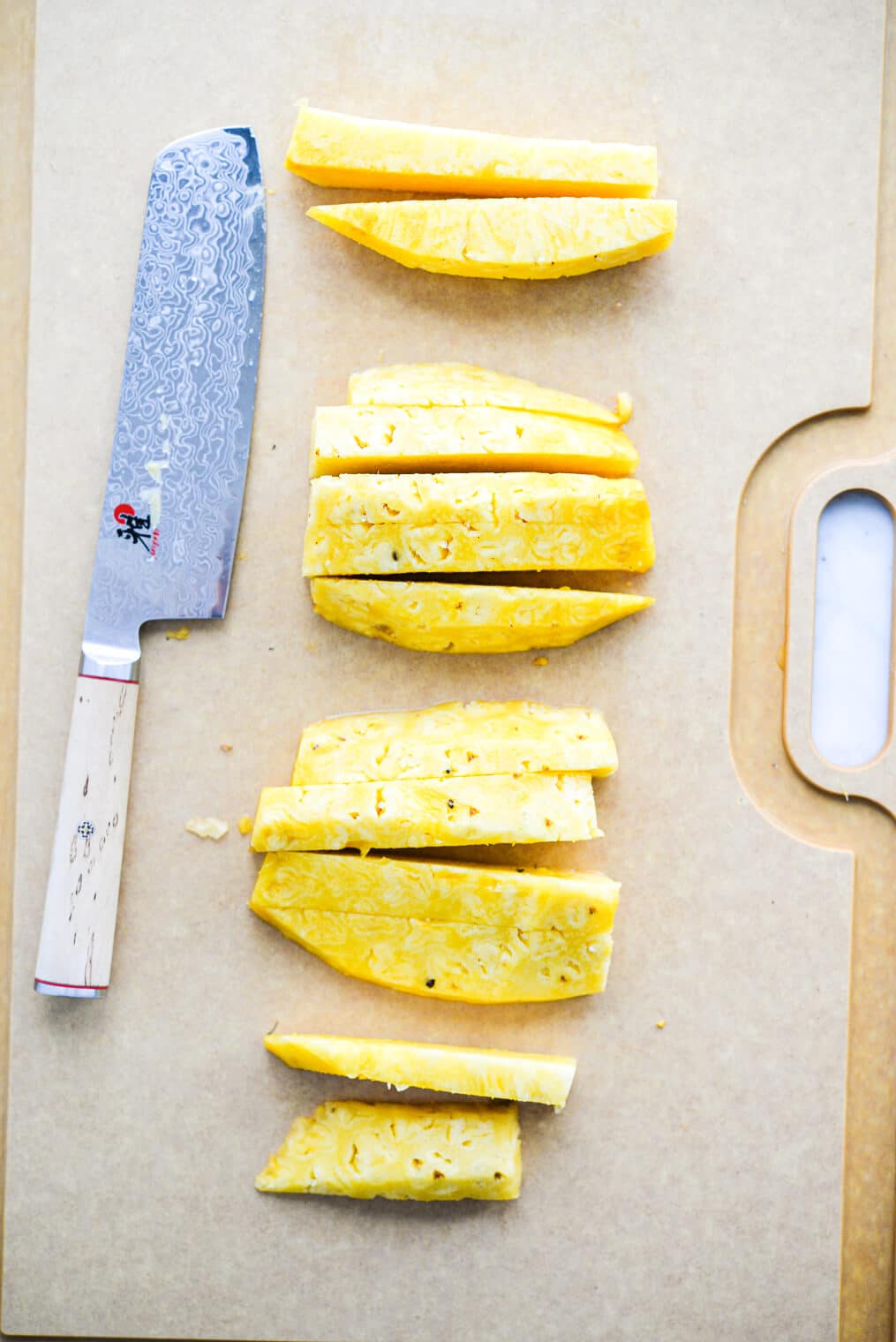 a large cutting board with sticks of fresh cut pineapple laying on it next to a large knife