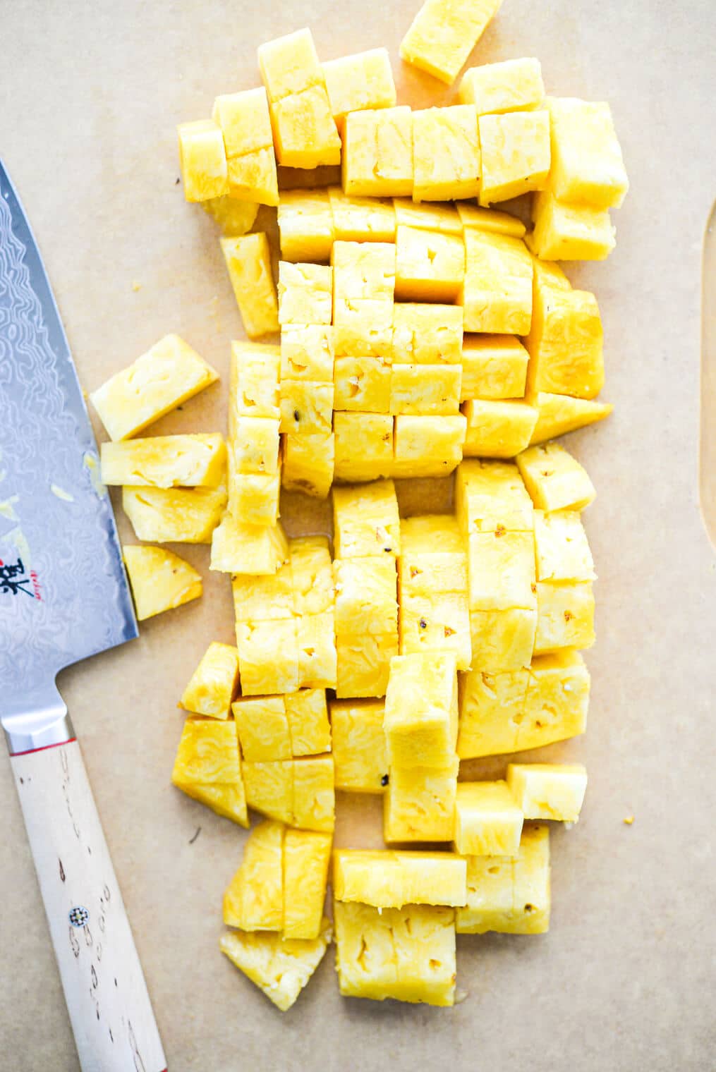 a large cutting board of cubed pineapple flesh sitting next to a large knife
