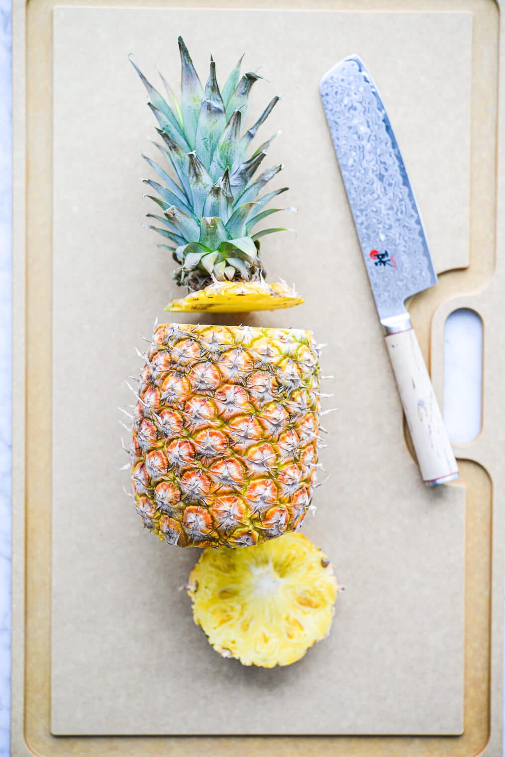 a pineapple laying on its side on a large cutting board with the bottom and the top of the pineapple sliced off