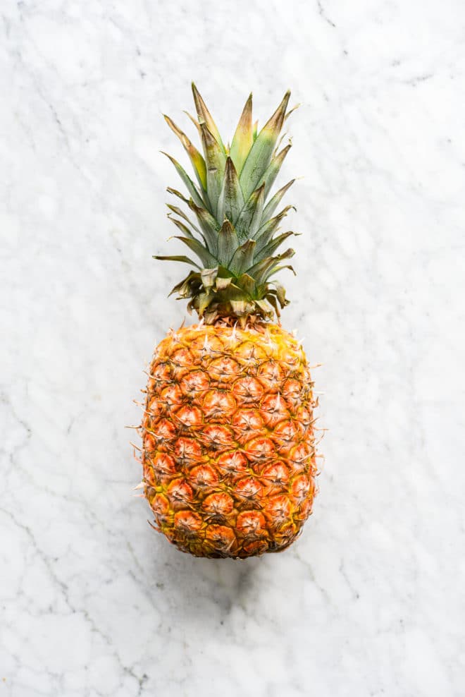 a whole, uncut pineapple laying on a marble surface