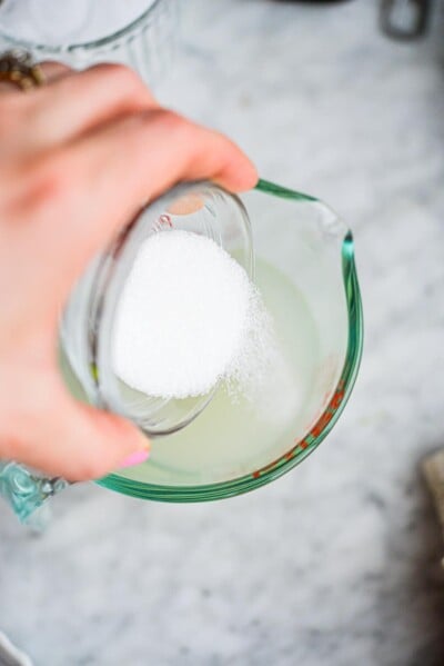 a woman pouring a small bowl of monk fruit sweetener into a measuring cup of keto margarita