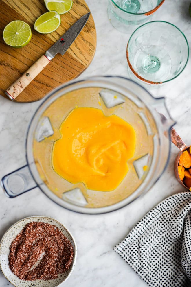 a top down photo of a pitcher of frozen mango margaritas surrounded by the other ingredients needed to make mango margaritas