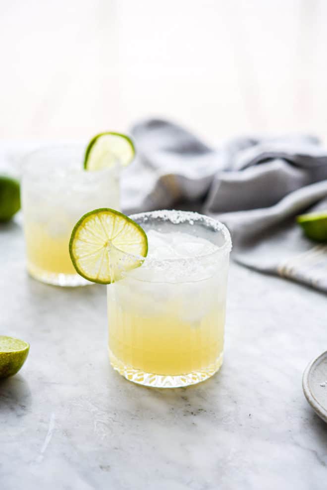 two salt rimmed glasses of skinny margarita sitting on a marble surface