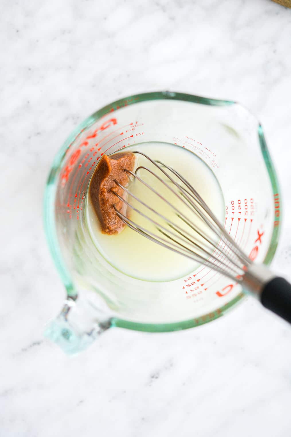 a measuring cup of lime juice and tamarind paste being whisked together