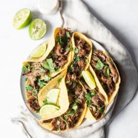 a plate of pork carnitas tacos garnished with lime wedges and cilantro