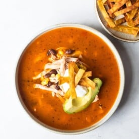 a bowl of creamy chicken tortilla soup garnished with avocado, sour cream, and fried tortilla strips