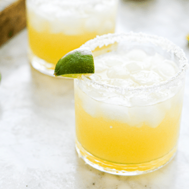 two salt rimmed glasses filled with margarita in front of sliced limes
