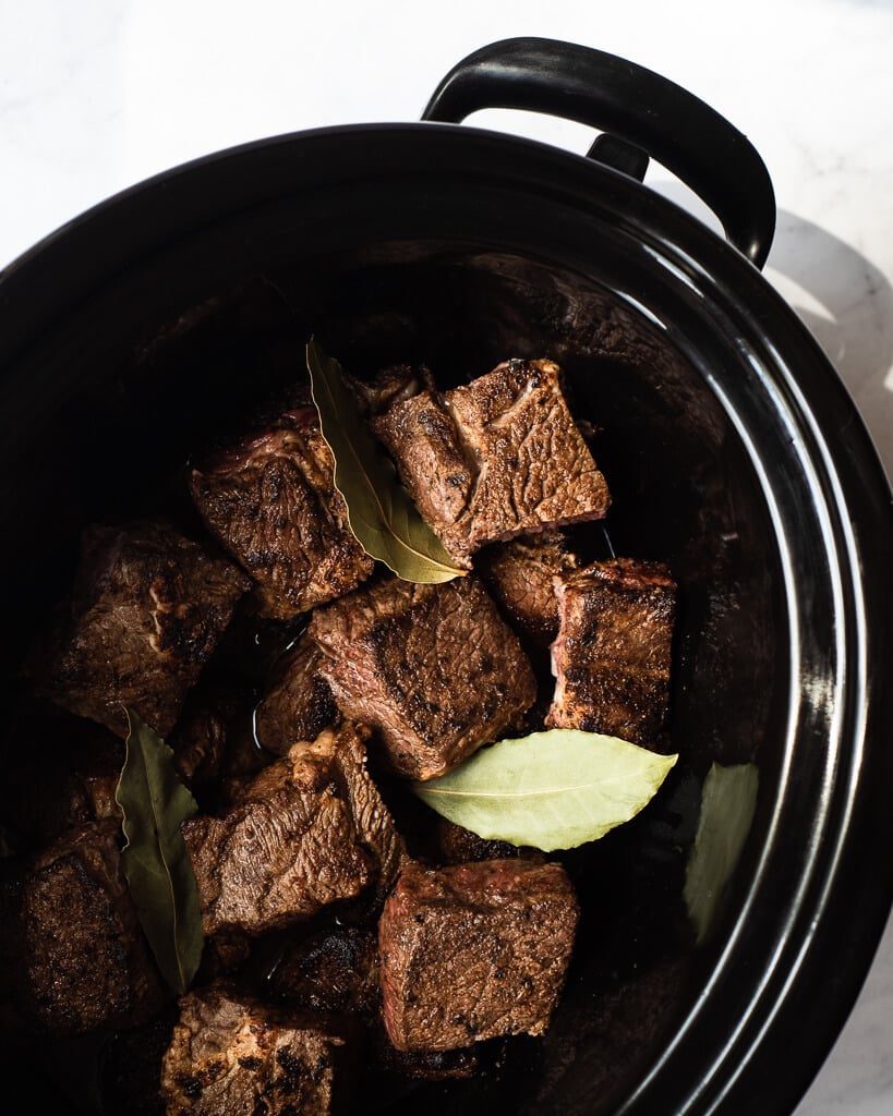 slow cooker filled with chunks of seared beef and bay leaves