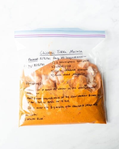 freezer meal chicken tikka masala in a labeled ziplock bag on a marble surface