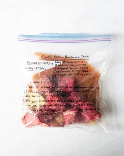 freezer meal slow cooker barbacoa tacos in a labeled ziplock bag on a marble surface
