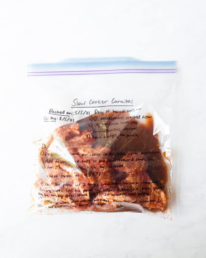 freezer meal slow cooker carnitas in a labeled ziplock bag on a marble surface