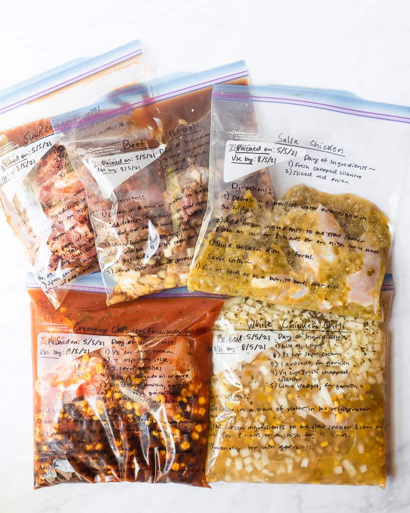 5 freezer meals in gallon size labeled ziplock bags laying on a white surface
