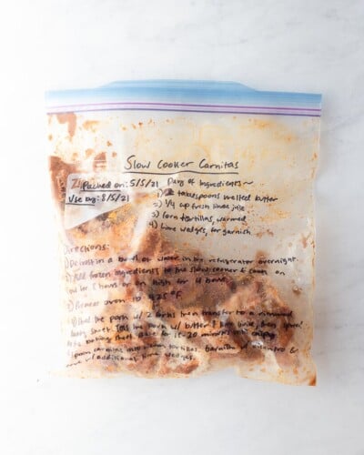 freezer meal slow cooker carnitas in a labeled ziplock bag on a marble surface