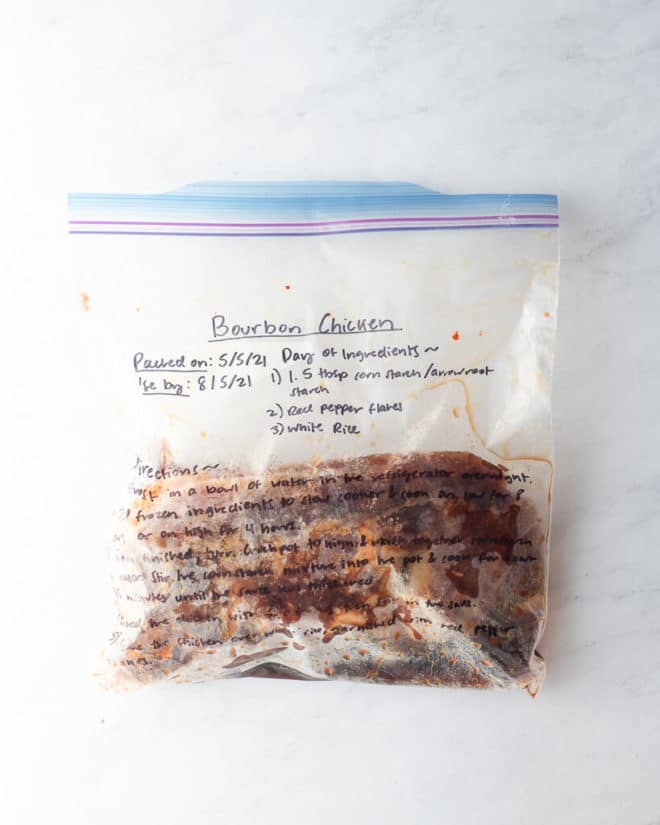 freezer meal bourbon chicken in a labeled ziplock bag on a marble surface