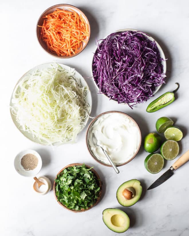 the ingredients for creamy Mexican coleslaw sitting on a marble surface