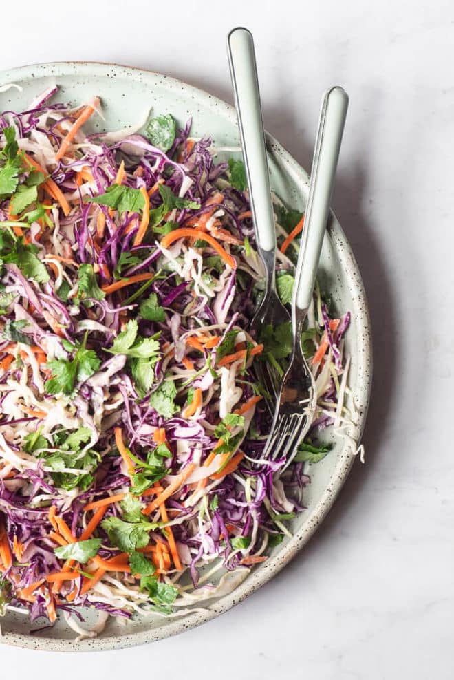 a plate filled with creamy Mexican coleslaw sitting on a marble surface