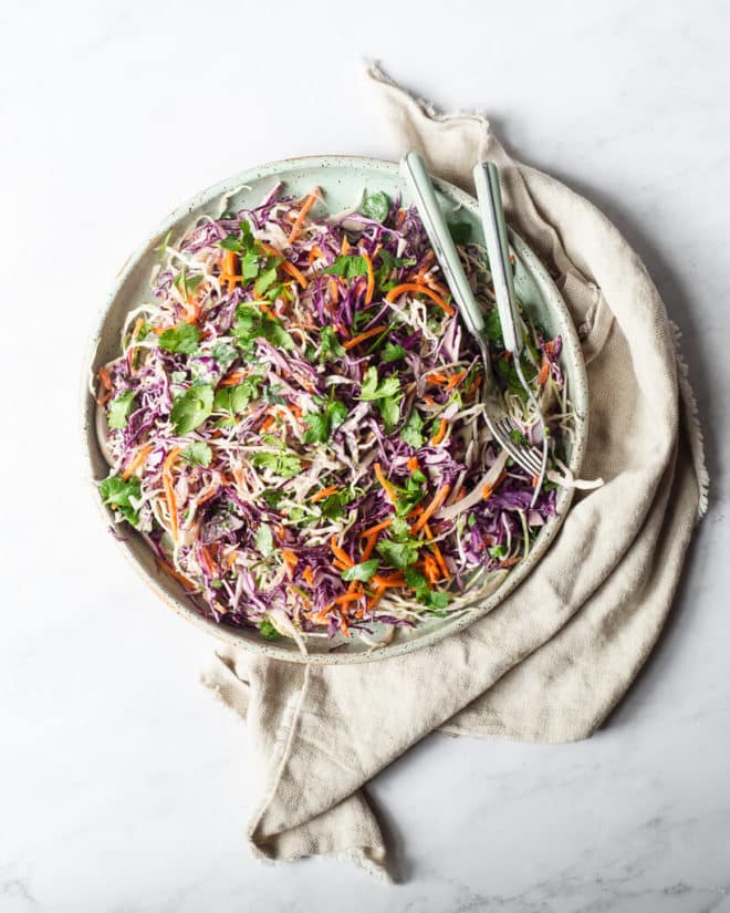 a plate filled with creamy Mexican coleslaw sitting on a tan kitchen towel on a marble surface