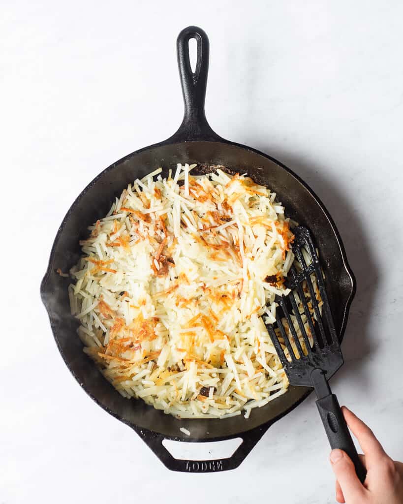 a person using a spatula to flip over browned shredded hash browns