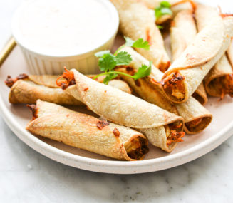 a plate of air fryer chicken taquitos and a small bowl of sour cream sitting on a marble surface