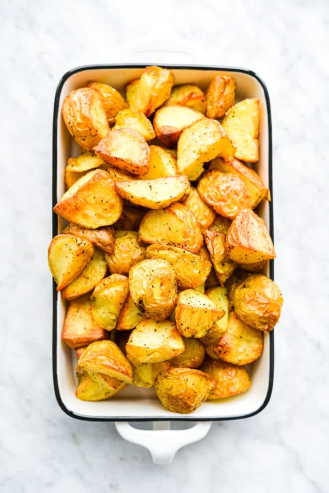 a small dish filled with crispy roasted potatoes sitting on a marble surface