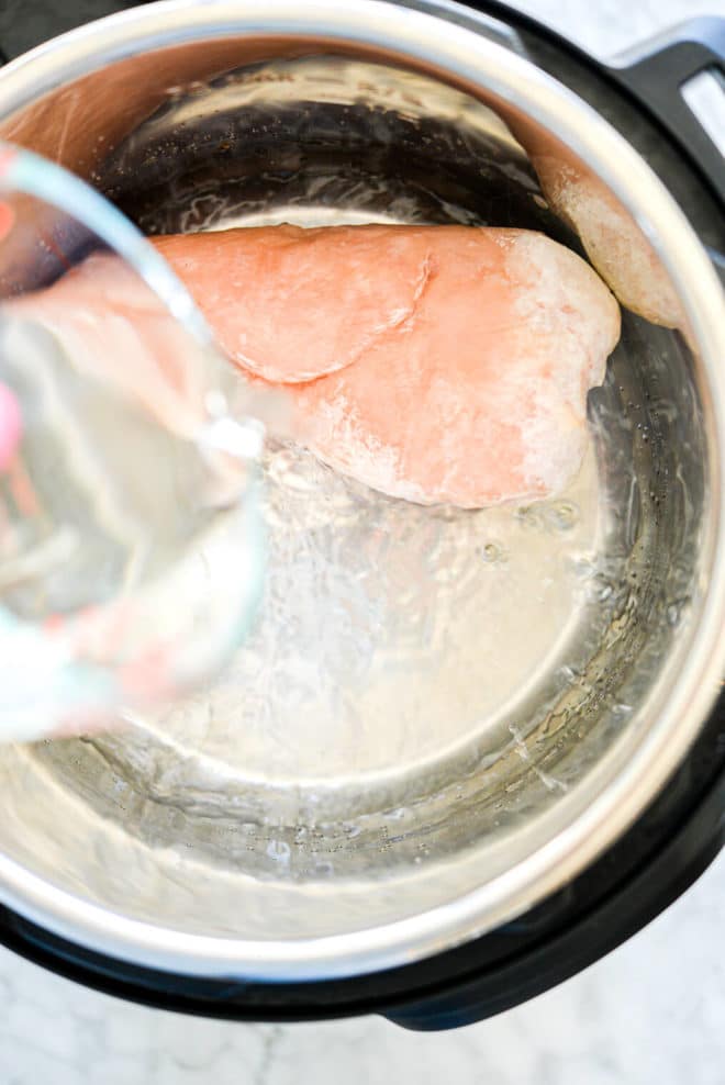 a big chunk of frozen chicken breast in an instant pot with someone pouring water over it