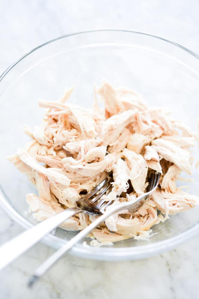 a small glass bowl of shredded chicken with two forks sticking out of the bowl